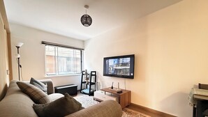 Una sala de estar moderna con un sofá, un televisor de pantalla plana montado en la pared, una lámpara de pie y una ventana con persianas.