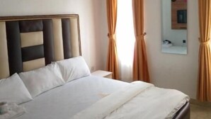 Una habitación de hotel con cama, cortinas, un espejo y un cuadro colgado en la pared.