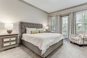 Ein Schlafzimmer mit einem großen Bett, zwei Nachttischen, einem Sessel und Blick ins Freie durch ein Fenster.