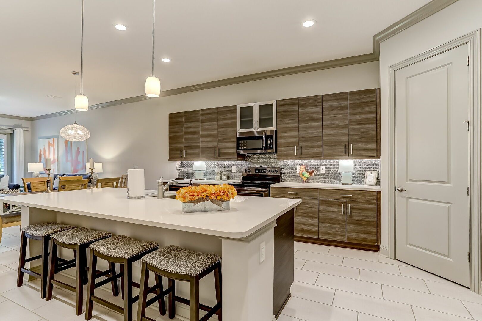 Una cocina moderna con una isla central, taburetes de bar, un microondas y un gallo decorativo.