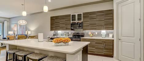 Una cocina moderna con una isla central, taburetes de bar, un microondas y un gallo decorativo.