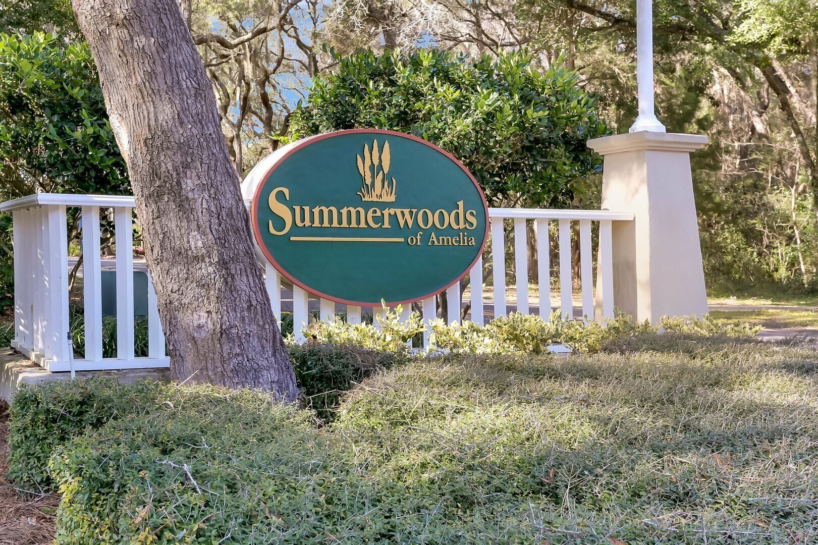 Señal de Summerwoods of Amelia, con una cerca blanca de piquetes y follaje al fondo.