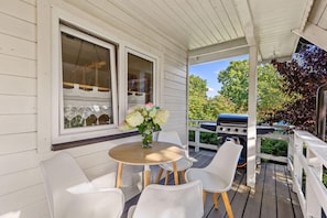 A covered porch with a table and chairs, a grill, and a window with a view of trees. - Large and Comfortable Holiday Home With a Terrace (Darlowo)