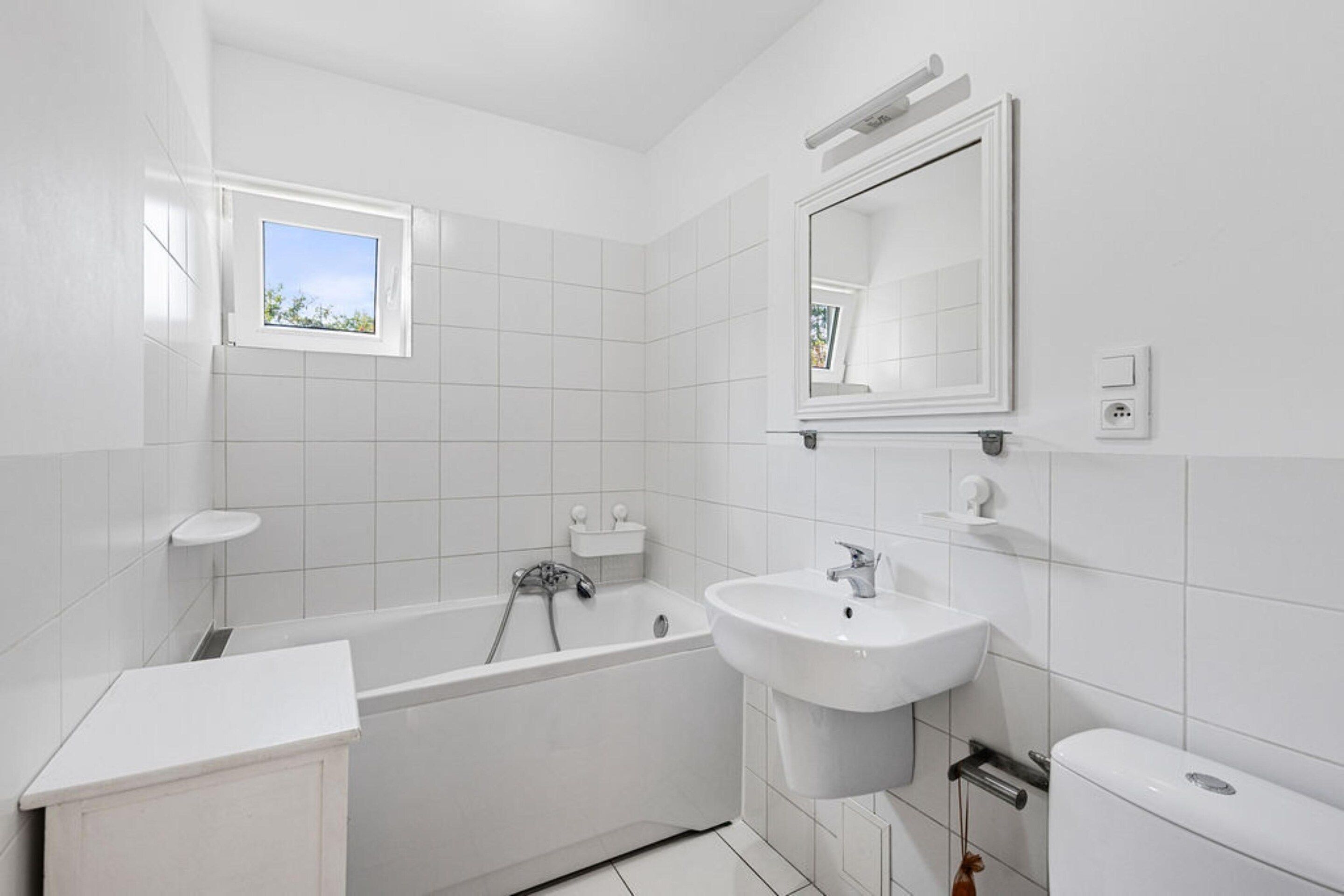 A modern bathroom with a bathtub, a sink, and a toilet. There is a window providing natural light.