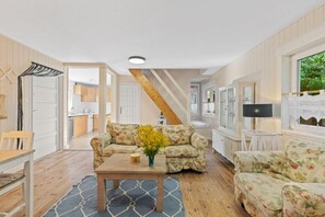 A cozy living room with a wooden floor, a floral sofa, a coffee table, and a view of the kitchen through an open door. - Large and Comfortable Holiday Home With a Terrace (Darlowo)