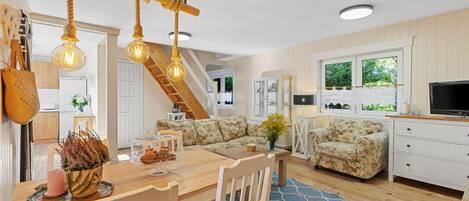 A cozy living room with a wooden dining table, floral sofa, and a TV on a white cabinet.