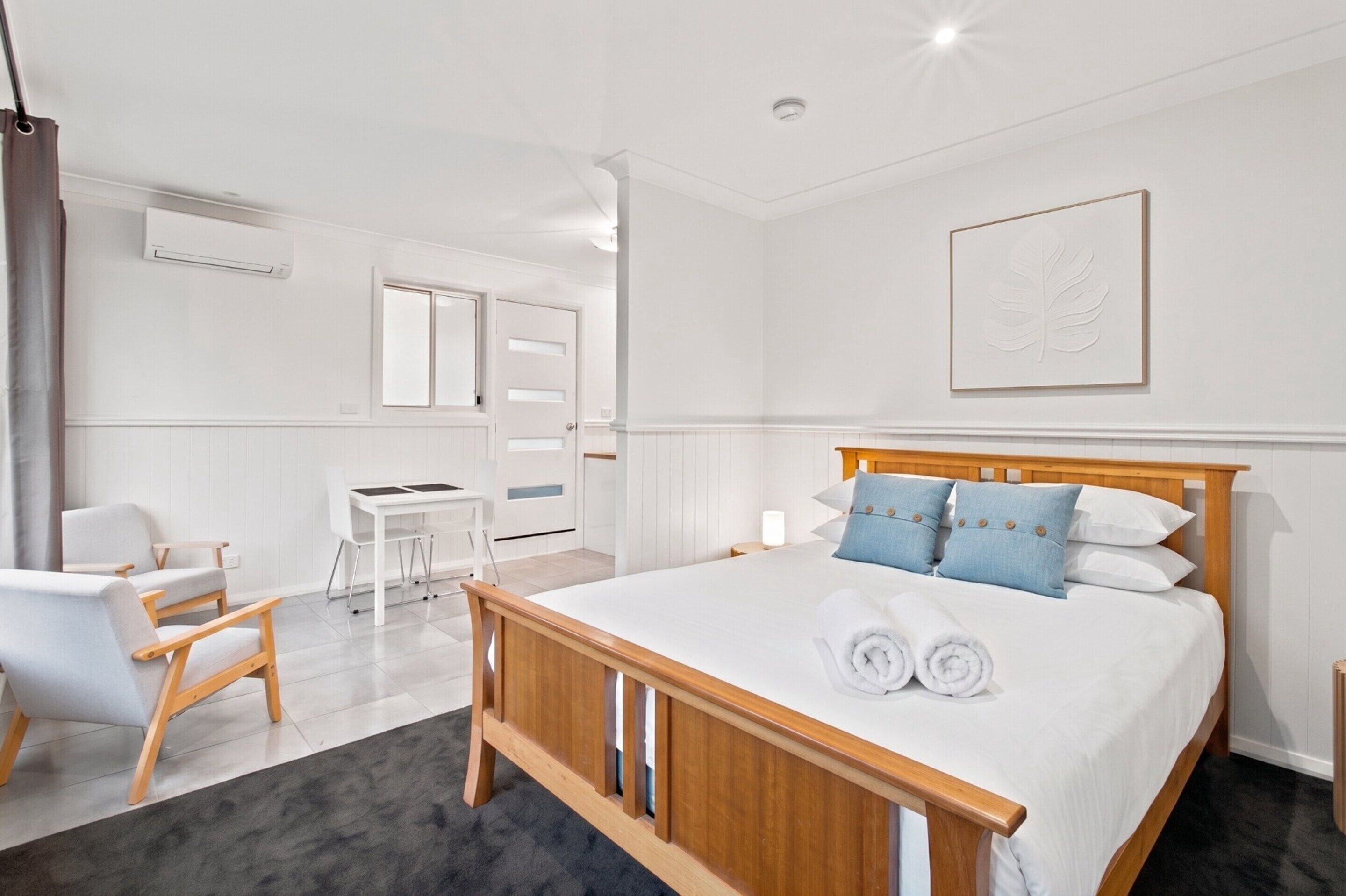 A hotel room with a wooden bed, a desk, a chair, and a large window.