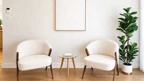 Twee fauteuils tegenover elkaar met een kleine glazen tafel ertussen, een lijst met abstracte kunst aan de muur, en een potplant aan de rechterkant.