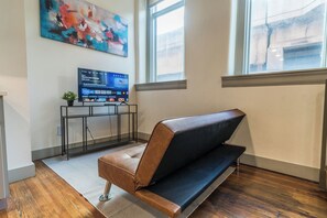Ein modernes Zimmer mit einer Lederecke, einem Flachbildfernseher auf einem Beistelltisch und einem großen abstrakten Gemälde an der Wand.
