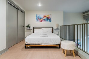 A bedroom with a bed, bedside tables, a painting, a plant, and a balcony railing. - Spacious Loft - Parking Nearby - DT - 2F (Louisville)