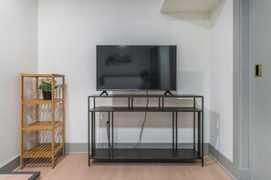 Ein modernes Wohnzimmer mit einem flachbildfernseher, der an einer schwarzen Metallkonsole befestigt ist, einem Holzregal mit einem Blumentopf und einem hellen Boden.