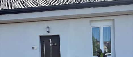 A building with a tiled roof, a door labeled '12', a small table with chairs, and potted plants.