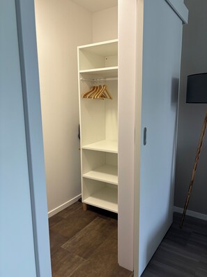 A walk-in closet with open doors, wooden hangers, and a floor lamp.