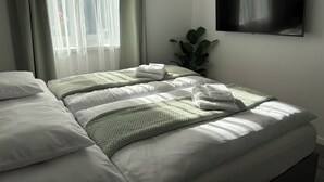 Une chambre d’hôtel avec un lit, un téléviseur fixé au mur et une fenêtre avec des rideaux légers.