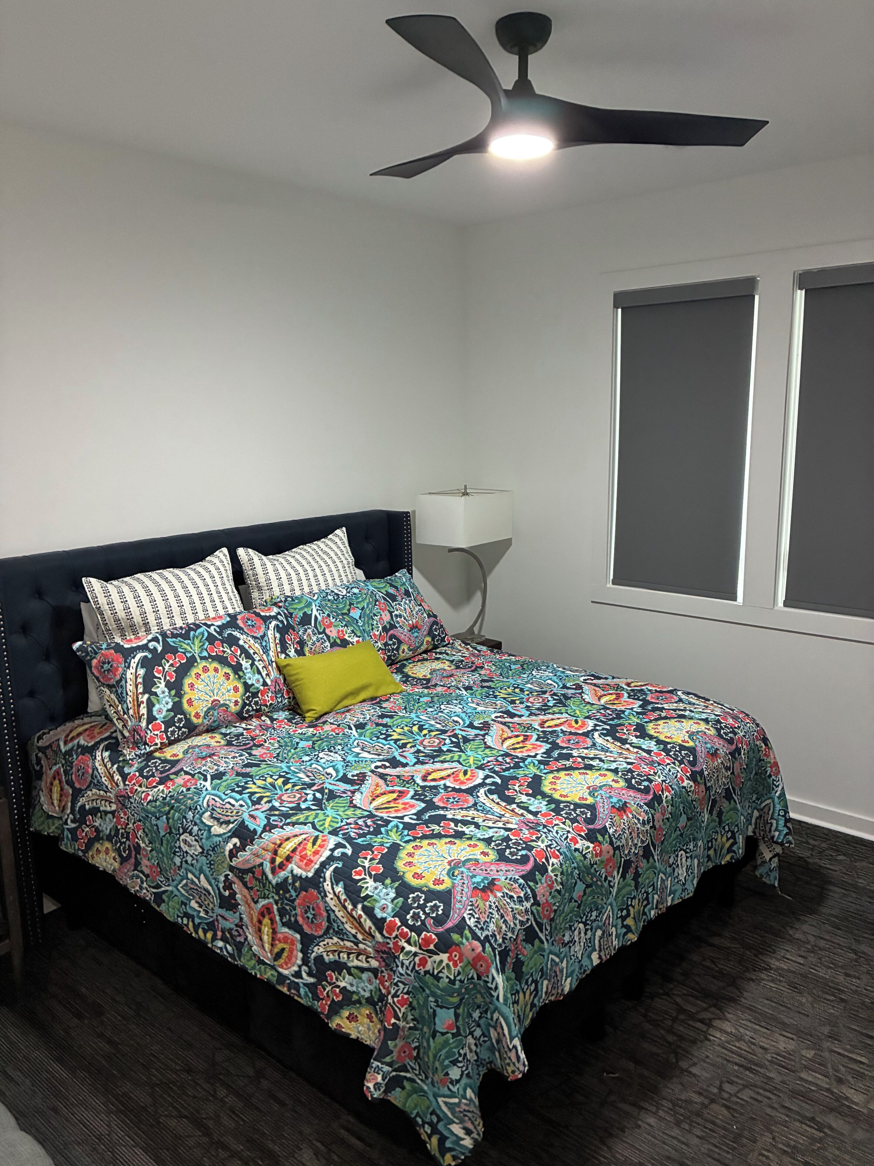 A bedroom with a bed, a ceiling fan, a window, and a nightstand.