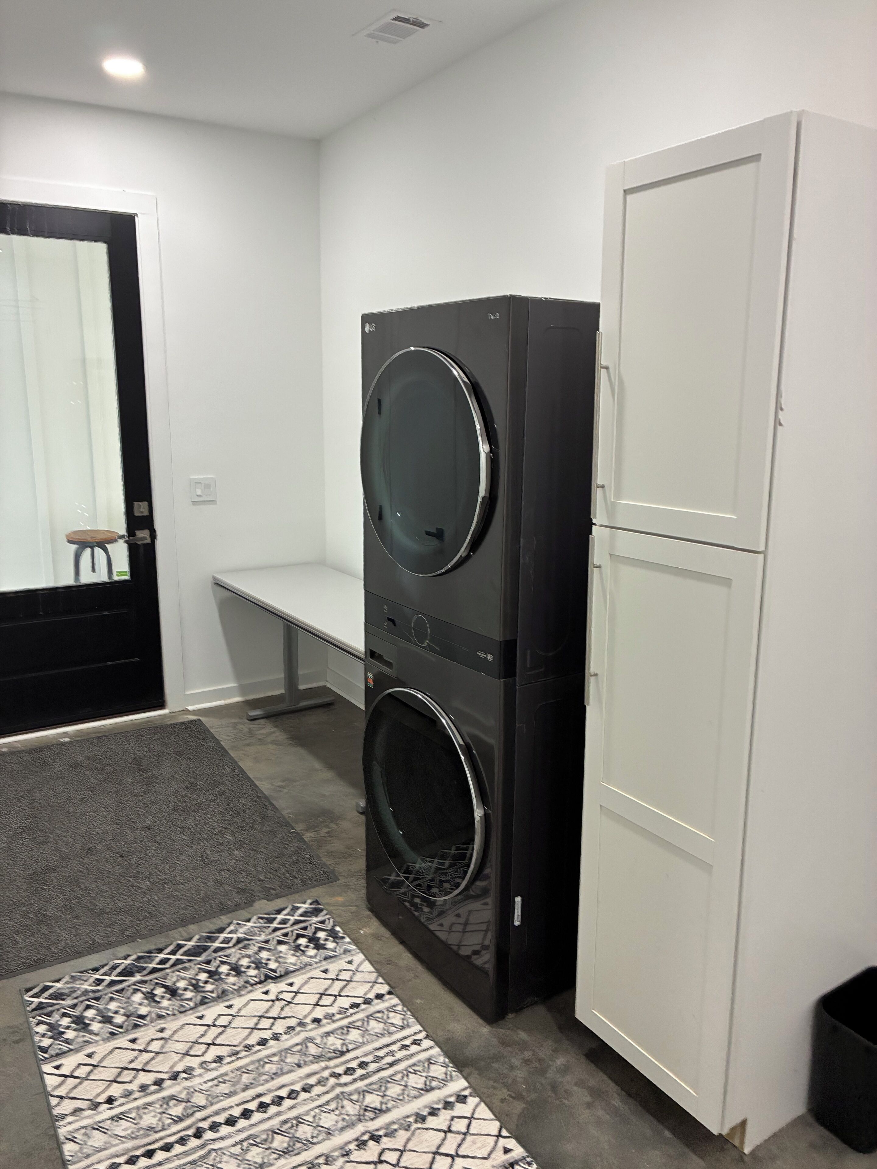 A laundry room with two stacked washers and dryers, a bench, and a patterned rug.