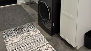A laundry room with two stacked washers and dryers, a bench, and a patterned rug. - Two bedroom underground space sits right on the water. (Eclectic)