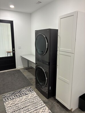 A laundry room with two stacked washers and dryers, a bench, and a patterned rug. - Two bedroom underground space sits right on the water. (Eclectic)