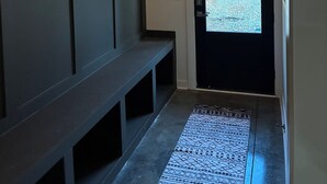 A hallway with a bench, a door leading outside, and a patterned rug. - Two bedroom underground space sits right on the water. (Eclectic)