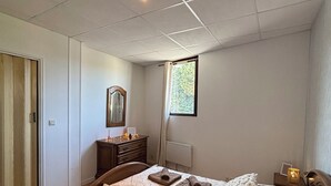 A bedroom with a bed, a dresser, a mirror, a window with curtains, and a nightstand with a lamp.