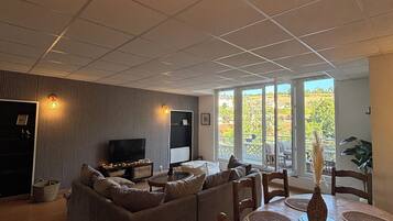Een woonkamer met een hoekbank, een flatscreen televisie en een eetgedeelte met een houten tafel en stoelen.