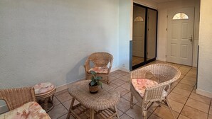 A sunlit patio with wicker furniture and a tiled floor.