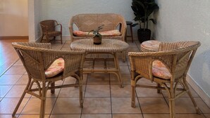 A room with a high ceiling, a tiled floor, and a seating area with wicker furniture and a small table.