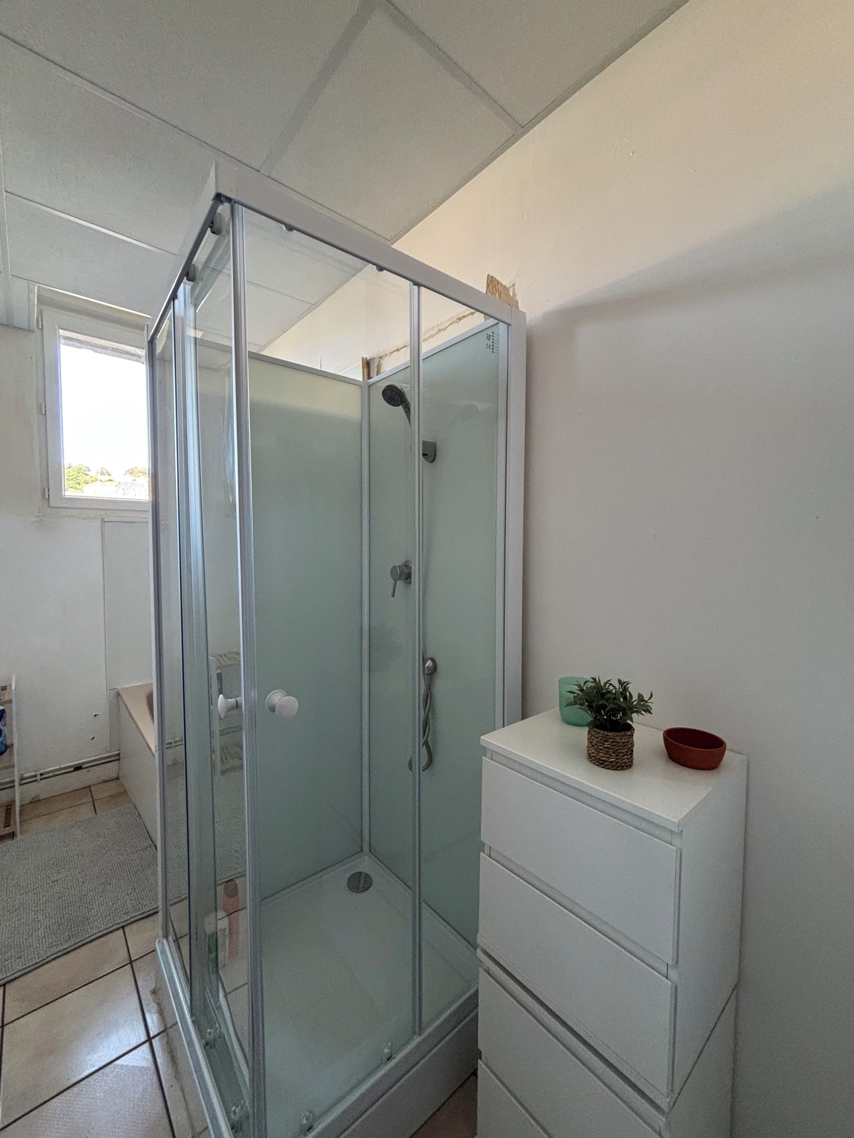 Une douche fermée par des parois de verre, avec un meuble blanc à côté.