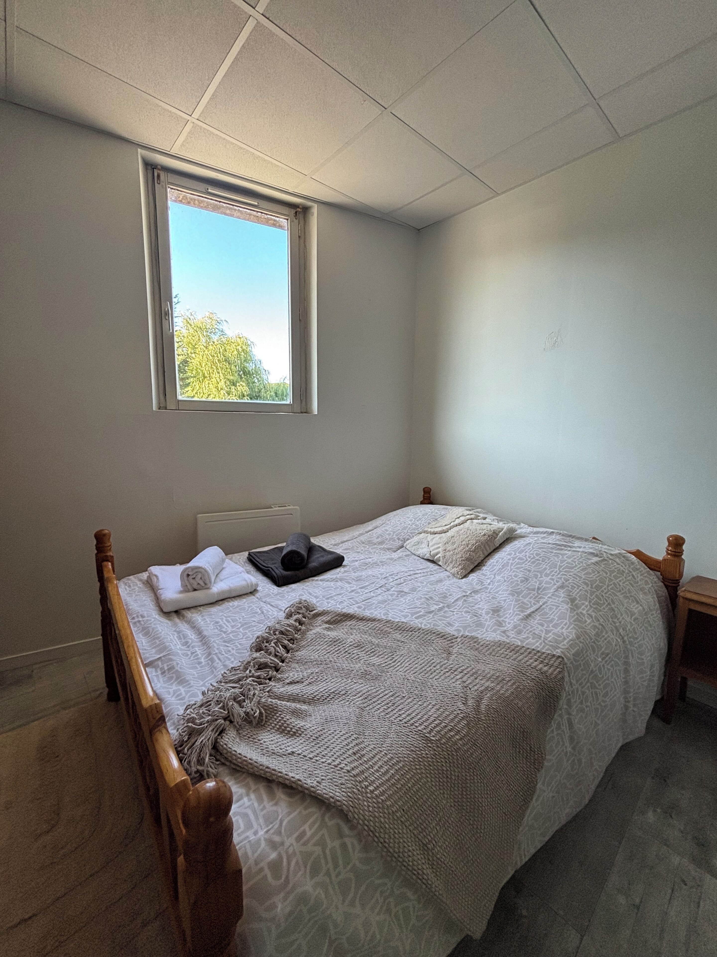 Un dormitorio con cama, ventana y mesita de noche.