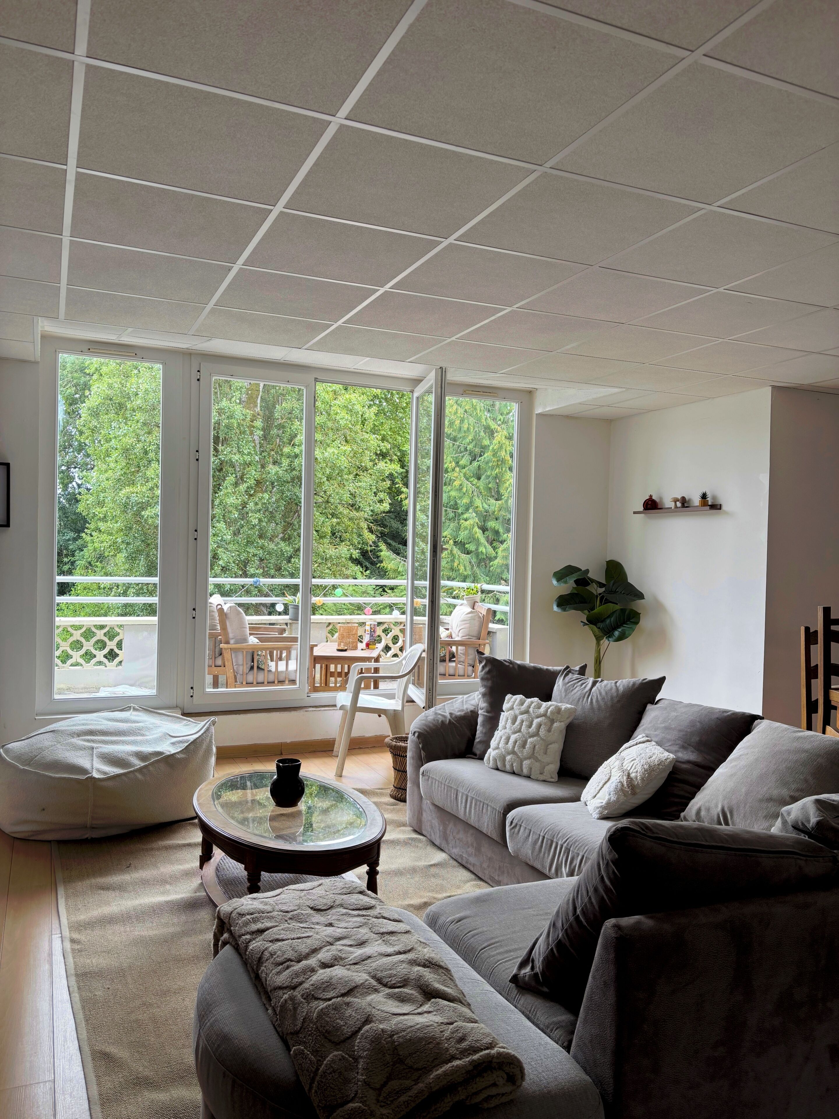 A modern living room with a sofa, a glass coffee table, and a large window with a view of greenery.