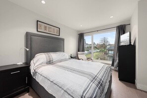 A modern bedroom with a large bed, a bedside table, a chair, a wardrobe, and a window with a view of the outside.