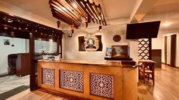 Un área de recepción con mostrador de madera, paneles decorativos, un reloj y una televisión.