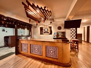 A reception area with a wooden counter, decorative panels, a clock, and a television. - Hotel O Kahilipara Nirvis Grand (Guwahati)