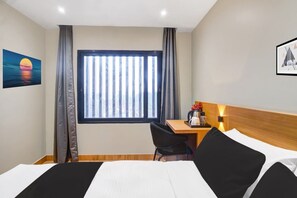 A hotel room with a bed, a desk, a chair, a window with vertical blinds, and a painting on the wall. - Hotel O Kahilipara Nirvis Grand (Guwahati)