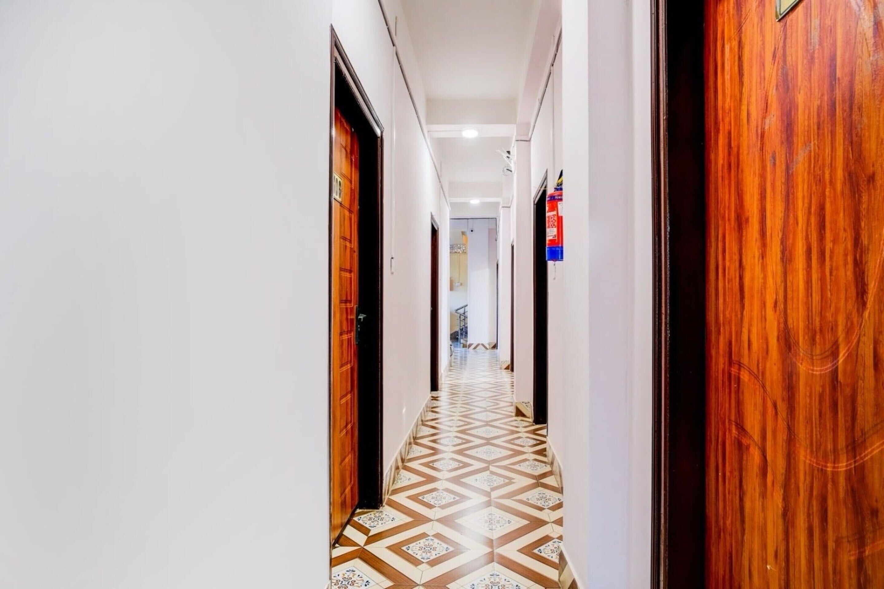 A hotel hallway with patterned flooring, wooden doors, and a fire extinguisher mounted on the wall.