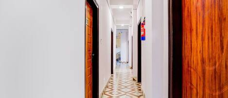 A hotel hallway with patterned flooring, wooden doors, and a fire extinguisher mounted on the wall.