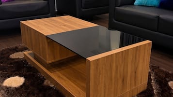 Una sala de estar moderna con una mesa de centro de vidrio, sofás negros y almohadones de colores.