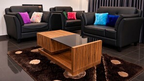 Een moderne woonkamer met twee zwarte leren banken, een houten salontafel en een vloerkleed met een patroon.