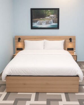 Een net opgemaakt bed met een houten hoofdbord, twee nachtkastjes met lampen, en een lijst met een foto van een waterval aan de muur.