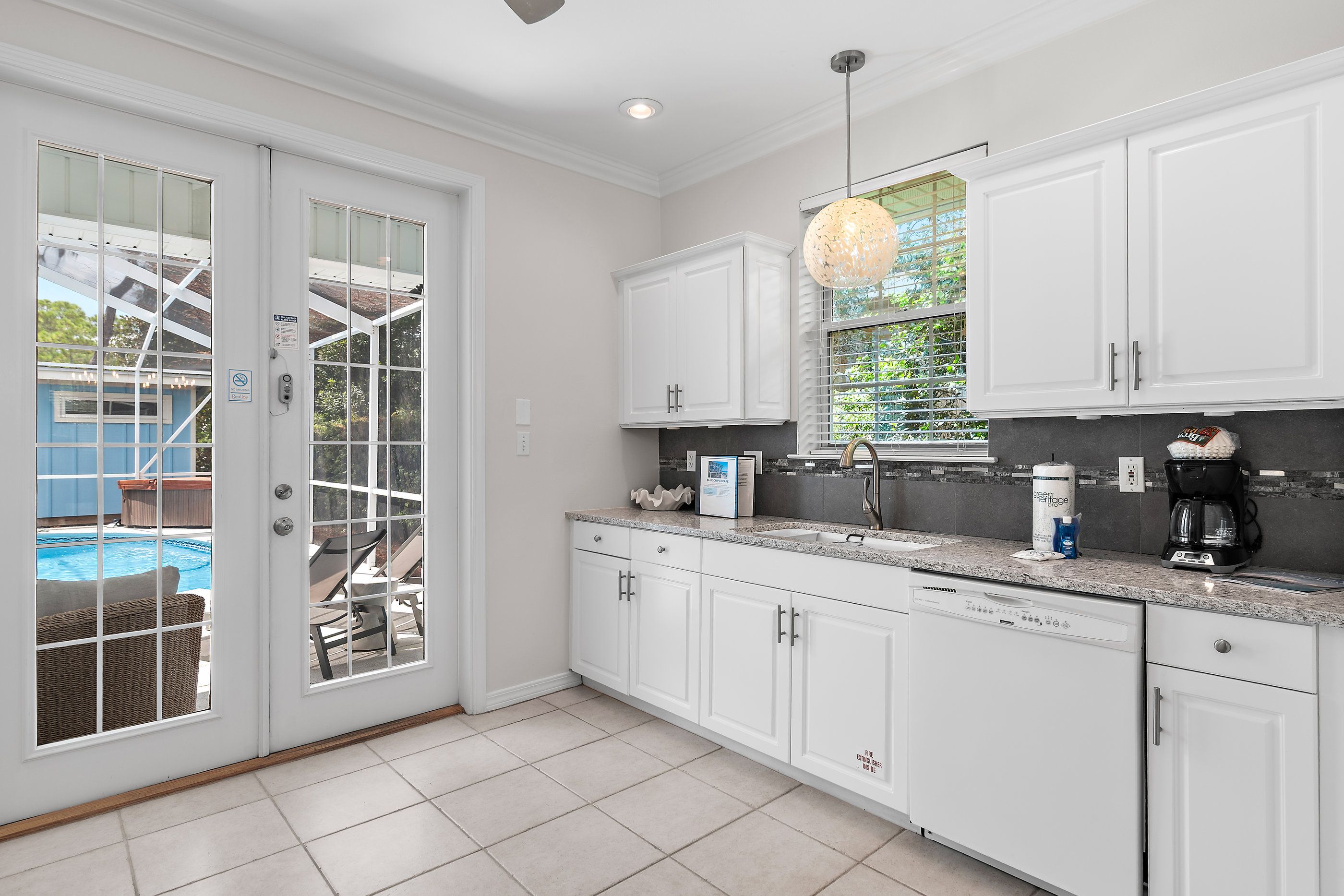 A kitchen with white cabinets, a granite countertop, and a view of a pool through a glass door.