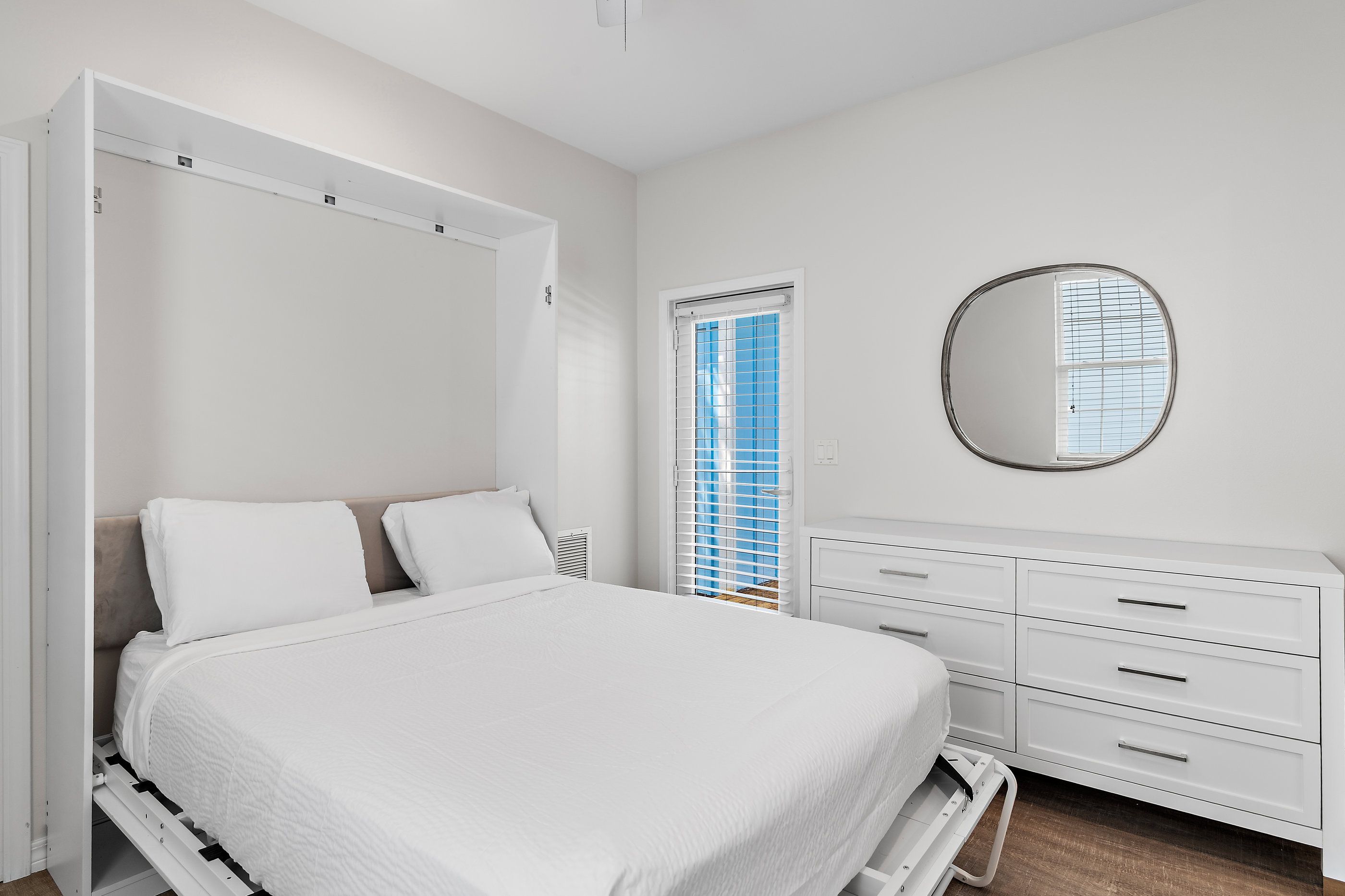 A bedroom with a bed, a wardrobe, a mirror, and a window with blinds.