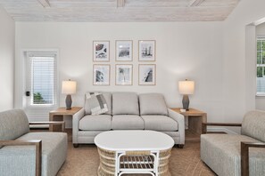 A living room with a sofa, two side tables, a coffee table, and framed pictures on the wall. - Blue Chip Escape-Private Pool-30A-Bikes (Santa Rosa Beach)