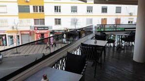 Un balcón con mobiliario exterior, con vistas a una calle con diversas tiendas y edificios.