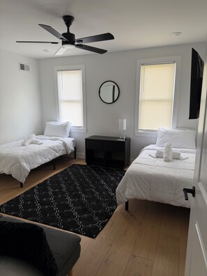 A bedroom with two beds, a ceiling fan, a small table, and a black patterned rug. -  Tacoma Family Haven Cozy Philly Getaway Close to I-76. Looking for convenience (Philadelphia)