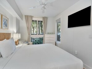 A bedroom with a large bed, a ceiling fan, a TV mounted on the wall, and a window with curtains. - 🏖️ Sandestin Retreat | 1BR pool level condo | hot tub | Baytowne 🐬 (Miramar Beach)