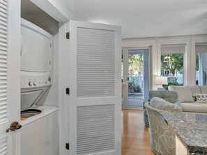 Ein modernes Interieur mit eingebauter Waschmaschine und Trockner, einer Sitzecke mit Sofa und Sesseln sowie einem großen Fenster mit Blick ins Freie.