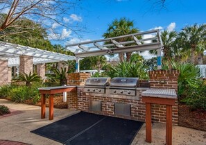 Ein Grillbereich im Freien mit einer Ziegelmauer, zwei Grills, einer Pergola und einem Ziegeltisch.