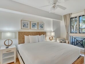 Ein Hotelzimmer mit einem großen Bett, zwei Nachttischen mit Lampen, einem Deckenventilator, einem Fenster mit Vorhängen und Bildern an der Wand.