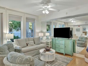Ein Wohnzimmer mit einer Couch, Sesseln, einem Fernseher, einem Couchtisch und einem Schrank.