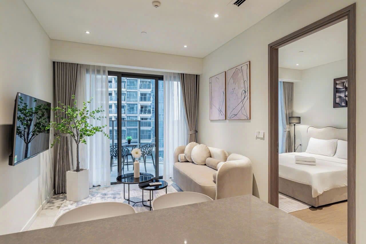 A modern hotel room with a sofa, a dining table, a TV, and a large window with curtains.